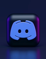 A 3D-style block with a blue logo in the center, set against a dark background. The logo resembles a game controller with two rounded edges and two circles on the front. The block has a subtle gradient, transitioning from dark to purple on its sides.